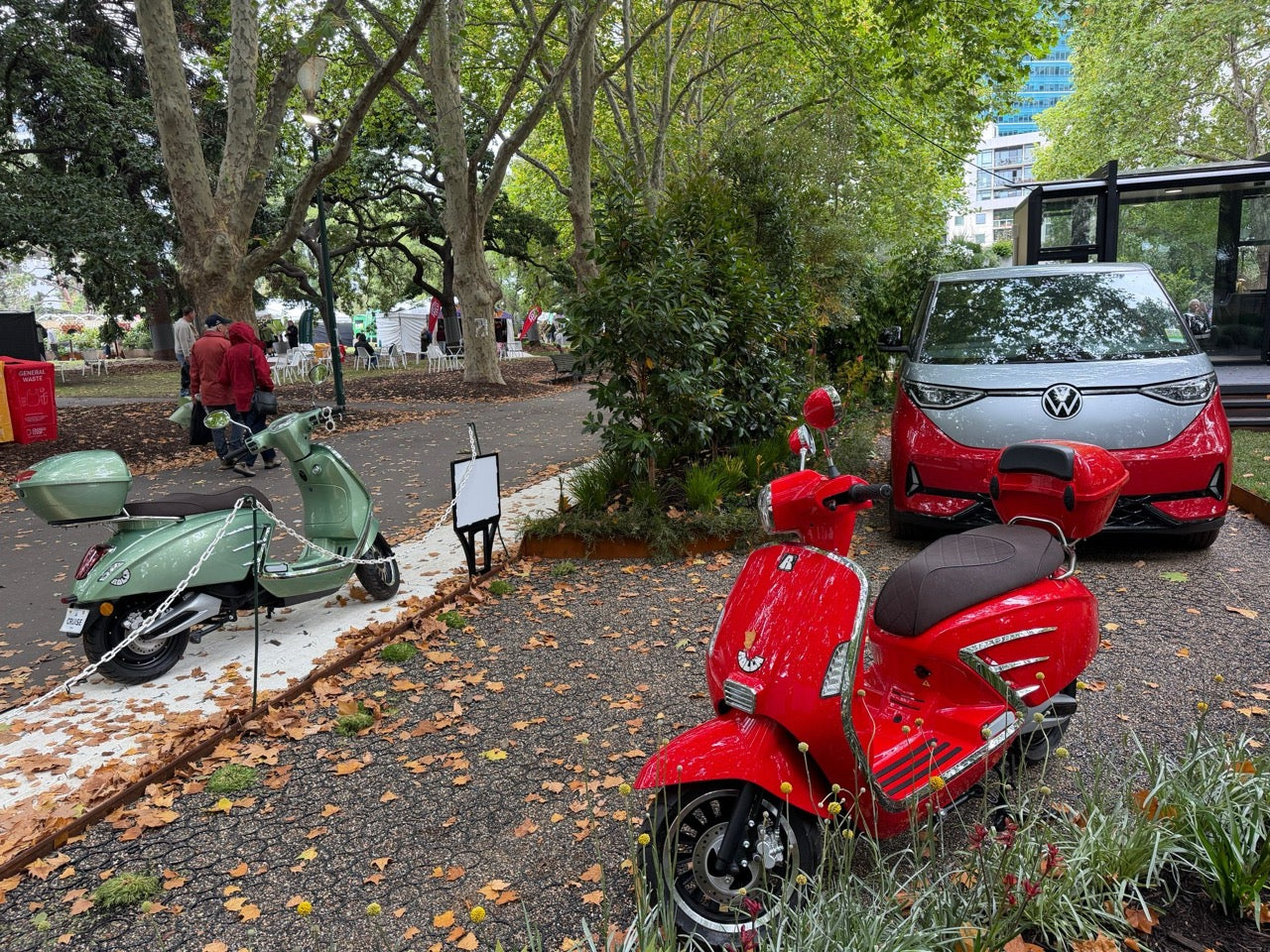 Red scooter parked on a street with trees and a car in the background